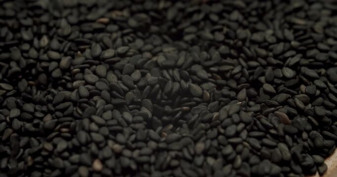 Macro shot of black sesame seeds cascading down in slow motion, creating a detailed texture of the healthy, natural, and organic condiment used in cooking and for making healthy oil
