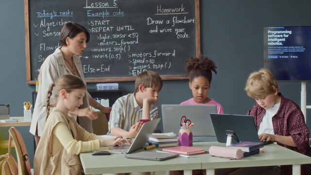 Diverse kids and female teacher coding on laptops during robotics lesson in classroom Clip is perfect for promoting STEM education, modern school curricula, and technology learning programs