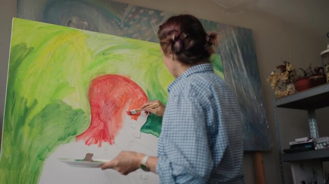 Talented woman artist painting an abstract picture on a large canvas, using a brush and a colorful palette in her bright and cozy studio, expressing her creativity and inspiration