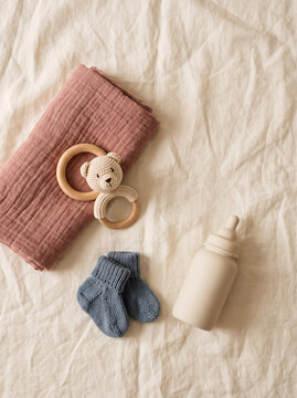 Soft newborn baby flat lay with a knitted mauve blanket, a wooden teether ring and tiny knitted socks on a cream background, gentle nursery still life with copy space