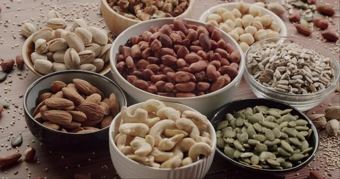Various types of nuts and seeds such as almonds, walnuts, hazelnuts, cashews, and pistachios displayed in ceramic and wooden bowls, representing a healthy and nutritious vegan snack.