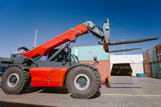 Orange Telehandler Lifts Its Forks Beside Stacked Shipping Containers at a Port Yard