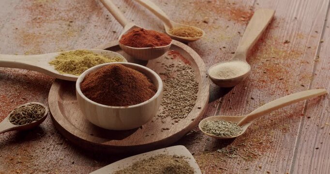 Flavorful assortment of various herbs and spices in wooden spoons and bowls, arranged on a rustic wooden table, perfect for culinary concepts and showcasing gourmet ingredients