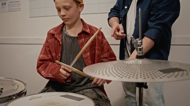 Tilt up shot of child practicing snare drum during music lesson while young instructor guiding him. Ideal for promoting music schools and youth education programs