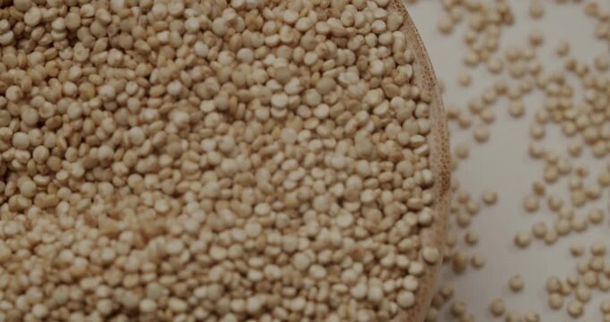 Raw white quinoa seeds rotating in wooden bowl. Close-up shot of a shiny metal spoon scooping up a pile of uncooked organic quinoa seeds in super slow motion, Healthy, organic, gluten-free superfood