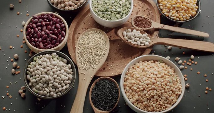 Colorful selection of raw uncooked legumes and grains displayed in bowls and spoons on a dark surface, highlighting various types of healthy plant-based protein sources for a balanced diet.