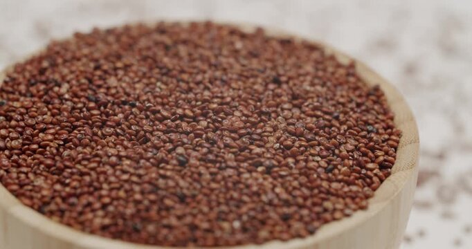 Uncooked red quinoa seeds filling a wooden bowl rotating in slow motion, highlighting the texture and color of the healthy, gluten-free pseudocereal grains in a detailed macro view.