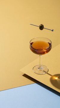 Midcentury coupe glass with floating olive on mustard blue backdrop
