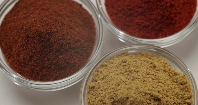 Aromatic spice powders rotating in glass bowls on a white background. Colorful aromatic ground spices like paprika, cumin, and chili rotating in small glass bowls. An assortment of herbs and spices