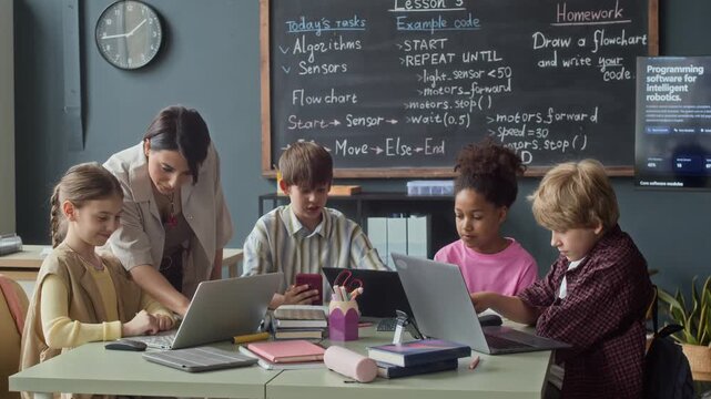 Multiethnic children learning coding and robotics with female teacher in classroom, using laptops. Footage is ideal for promoting STEM education programs and modern school curricula
