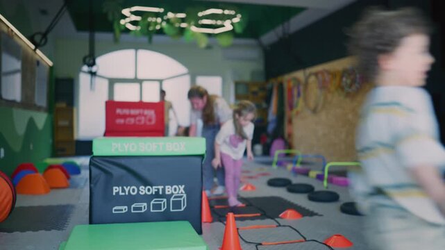 Children engage in active fitness training and exercises inside a vibrant indoor gym. Kids are developing coordination and agility using specialized equipment.