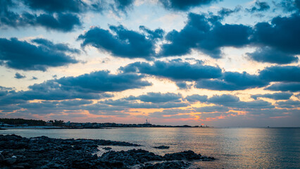 Obraz premium Dramatic dark clouds over a calm ocean and rocky volcanic coastline during a beautiful colorful sunset.