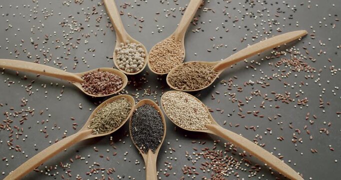 Various healthy seeds and grains rotating in wooden spoons. Variety of fresh seeds and grains in wooden spoons rotating on a gray surface, Wooden spoons with various grains and seeds rotating