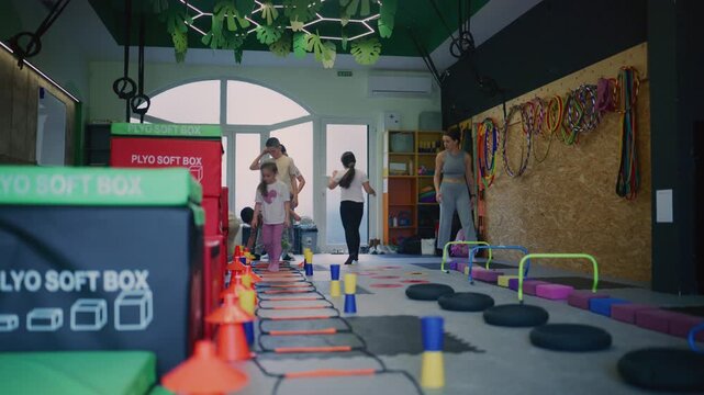 Young children are actively participating in a dynamic fitness and agility training session in a modern gym.