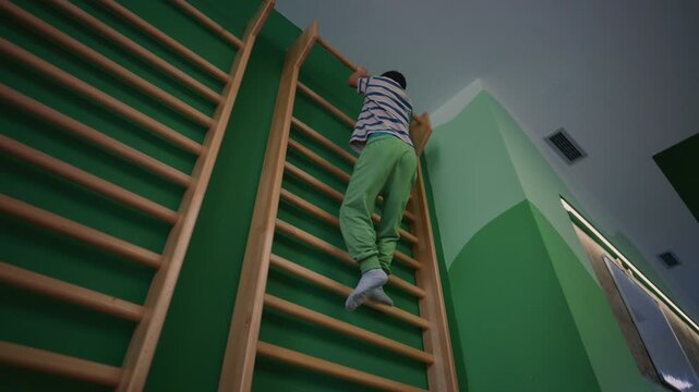 A young boy demonstrates his physical fitness by actively climbing a wall bar in a vibrant green gym. This active child enjoys exercising and developing his strength on the gym equipment.