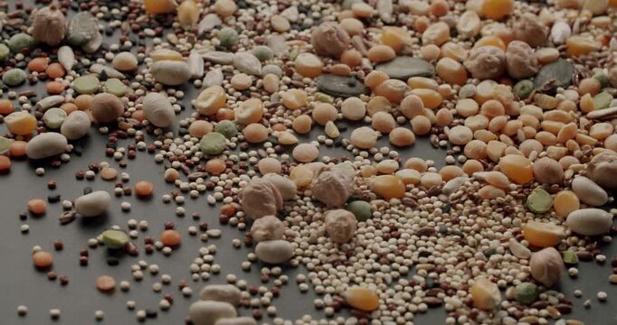 Super slow motion shot of various raw legumes and cereals falling and bouncing on a dark surface, showcasing a mix of chickpeas, lentils, peas, and quinoa for a healthy and nutritious meal