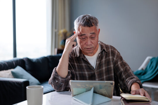 Senior man contemplates with digital tablet and notebook.