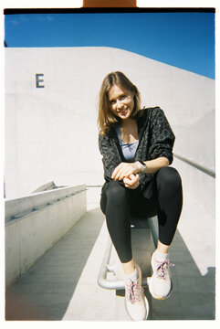 Young woman sits on a metal railing at a modern building