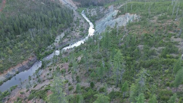 Aerial view of a river running through a valley in Southern Oregon on a Oregon summer evening showcasing evergreen trees, and washed out rockslides and a gravel bar. 