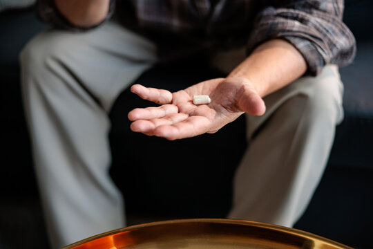 Elderly man holds medication capsule in his hand.