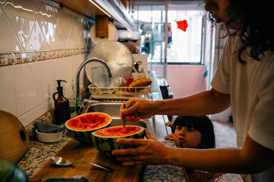Cutting Watermelon in a Kitchen With a Child Watching Nearby