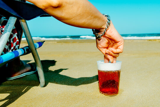 seated in a beach chair, a man dips two fingers into beer cup