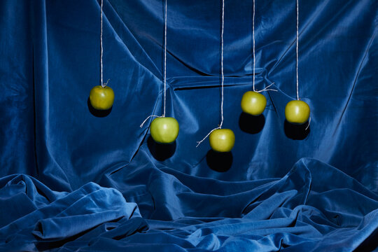 Five Green Apples Hang Against a Blue Velvet Background