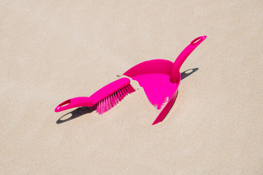 a close-up of a bright pink dustpan and brush covered by fine sand