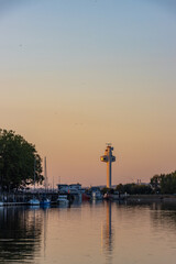 Obraz premium Modern harbor control tower and boats in Honfleur, Normandy, reflected on calm water during a warm sunset. Serene French maritime landscape.