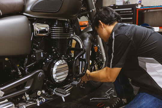 Motorcycle Mechanic Performing Maintenance on Motorcycle Engine in Repair Workshop