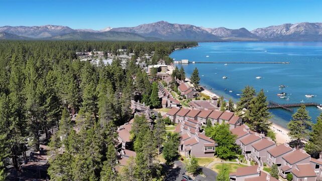 Aerial drone tracking shot flying forward over a Lake Tahoe beachside community with vacation properties, houses, and boats moored in the marina