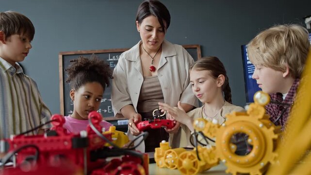 Multiethnic children and female teacher testing robotic models with remote control during STEM class. Perfect for educational marketing, school promos, and technology learning campaigns