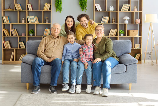 Family grandparents parents children smiling happy portrait together. They sit on a cozy sofa at home, ideal for ads about family life, bonding, care, and support. Concept shows family unity.