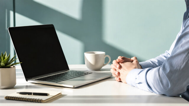 man sitting at desk with laptop. Professional employee with folded hands waiting before business meeting. Corporate work environment with coffee cup and notebook for productive day