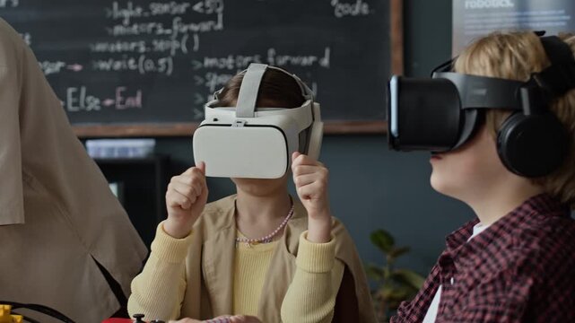 Caucasian children wearing VR headsets gesturing during robotics lesson while female teacher assists. Ideal for showcasing STEM education, modern school technology, and interactive learning