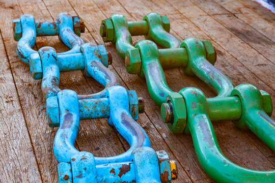 Row of heavy duty industrial colorful steel lifting shackles laid out on a ship wooden deck surface