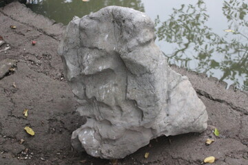 Natural textured gray stone boulder placed on muddy ground near reflective water. © HDStudios