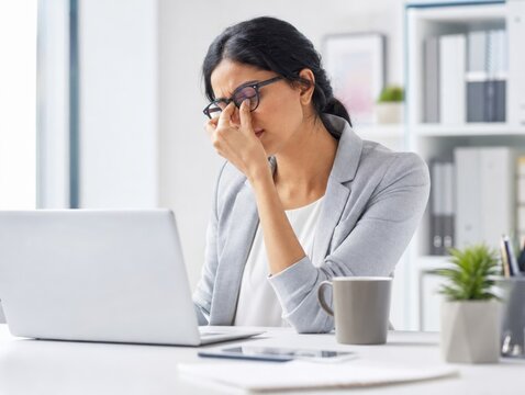 Stressed businesswoman feeling overwhelmed and tired while working on laptop in bright office with stressed