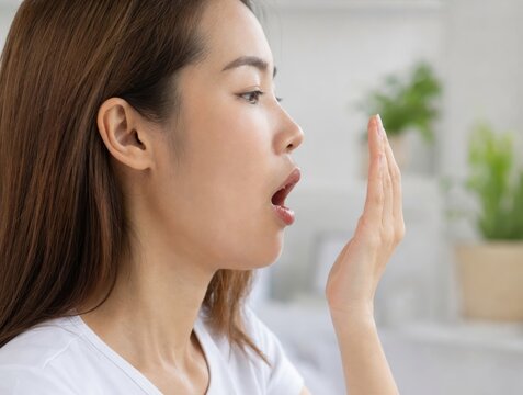 Young woman checking her breath by blowing into her hand to test for freshness with self care, health consciou