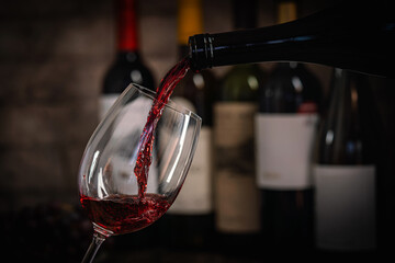 Obraz premium A dark, elegant still life of red wine being poured into a glass with wine bottles and fresh grapes in the background. Perfect for wine-themed compositions