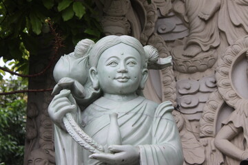 Fototapeta premium Jade colored statue of young female figure holding lotus flower and small vessel.