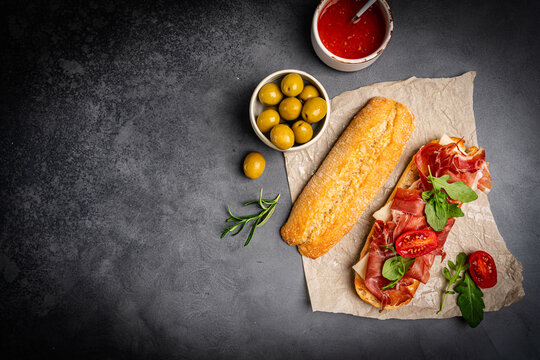 Grilled toast with jamon or prosciutto, tomatoes and fresh arugula leaves on the plate on dark background for breakfast top view. Healthy homemade breakfast or lunch idea.