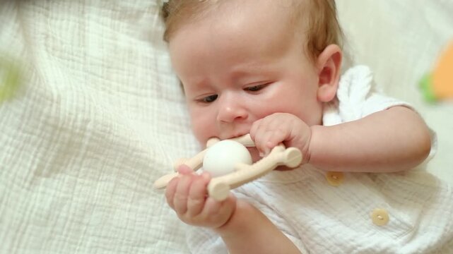 A sweet baby lies on a soft blanket, chewing on a silicone teether. A realistic portrait of a baby's teething process at home