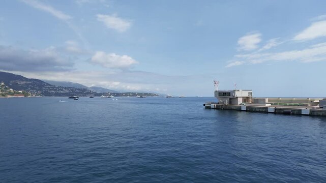 Monte-Carlo, Monaco ― 09.06.2026: Wide shot starting static on the Port Hercule office pier, with the camera briefly panning right and then reversing to slowly pan left, revealing the scenic Monaco co