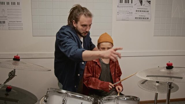 Male teacher instructing kid on playing drums during music lesson. Footage for promoting music schools, private tutoring, and creative youth education programs