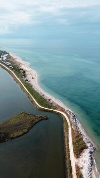 Vertical aerial view of a narrow road separating a blue sea and a dark lagoon lake