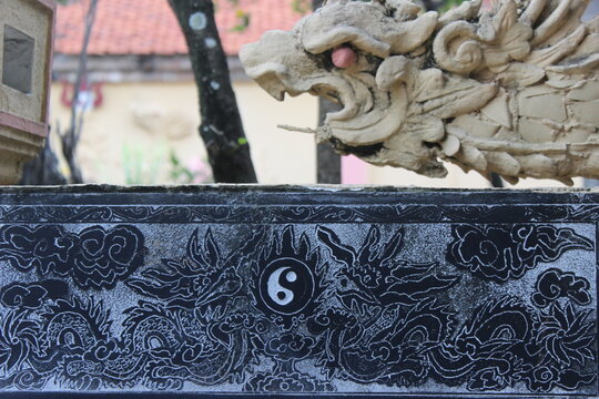 Stone dragon statue ornament with traditional yin yang symbol carved on black wall.