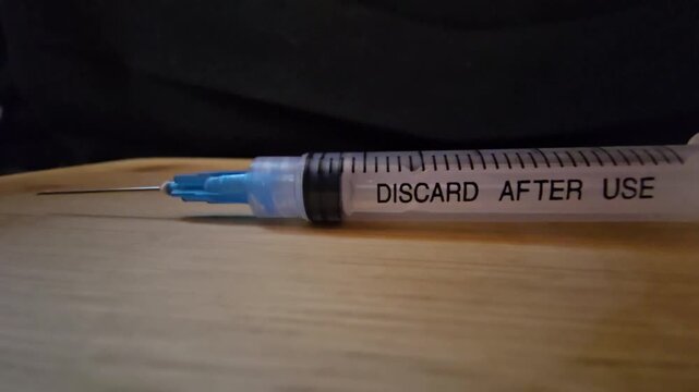 A close-up view of a medical syringe with a blue needle tip resting on a wooden surface, highlighting clinical precision and healthcare equipment.