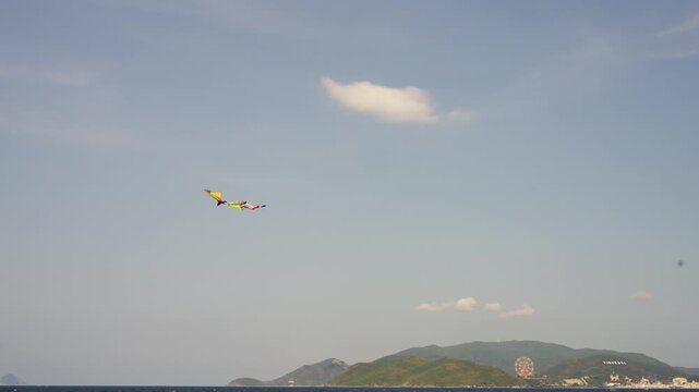 Middle of clip captures colorful kite soaring in upper-left quadrant drifting rightward over calm sea toward green shoreline; single small cloud floats near kite against.