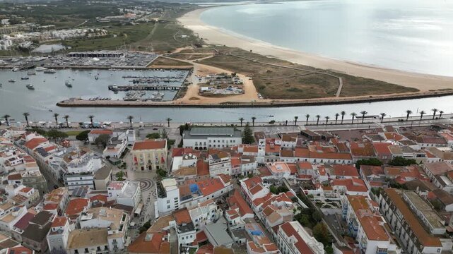 High-altitude drone footage of Lagos, Portugal, with city, sea, marina, sandy beach, rooftops and cloudy coastal atmosphere, perfect for destination marketing.